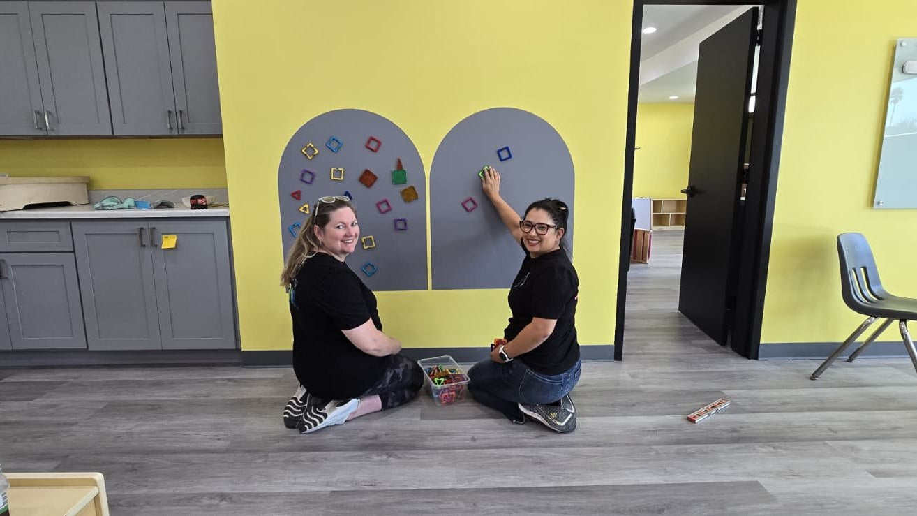 Olivia Martinez-Hauge and Amanda Staples installing sensory features on a magnetic wall.